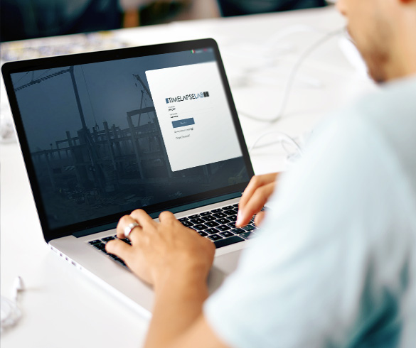 Una persona al computer di cui si vedono chiaramente solo le mani che scrive al computer. Sul monitor del computer è visualizzata la schermata di accesso al software di monitoraggio