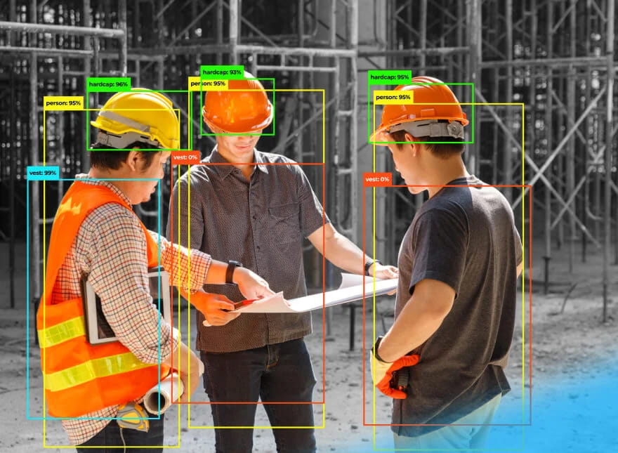 Tre operatori di cantiere stanno parlando tra loro mentre osservano una planimetria, sullo un cantiere. Sono presenti con diversi colori dei delineamenti di diverse aree dell'immagine che indicano elementi di conformità o meno alle norme di sicurezza (verde, giallo o rosso a seconda del grado)